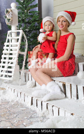 Mom and daughter in Santa's suits are sitting under snow Stock Photo