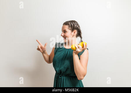 Stunning woman points to a invisible sign while holding fruits in her hand Stock Photo