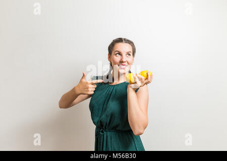 Lovely girl points to fruits and lemons and looks to side on white background Stock Photo