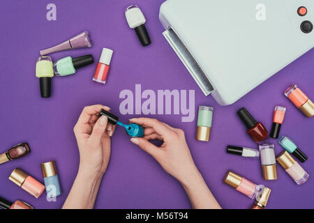 cropped image of woman holding turquoise nail polish isolated on purple Stock Photo