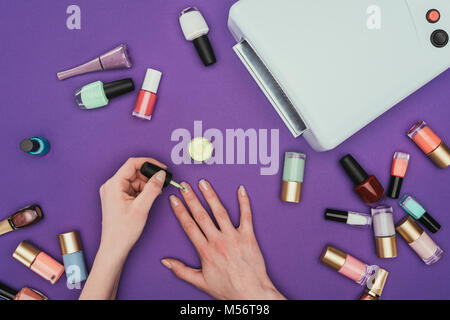 cropped image of woman painting nails isolated on purple Stock Photo