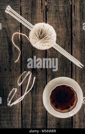top view of knitting needles, yarn, cup of tea and eyeglasses on wooden background Stock Photo