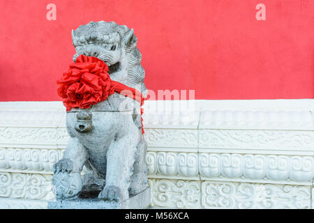 Traditional stone statue of a chinese guardian lion (male), wearing a big red bow around the neck to celebrate the chinese new year, posted in front o Stock Photo