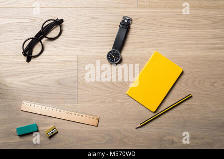 Gathering of office objects such as yellow notebook, ruler, pencil and rubber with black glasses and watch lying on office desk as flat lay from bird' Stock Photo