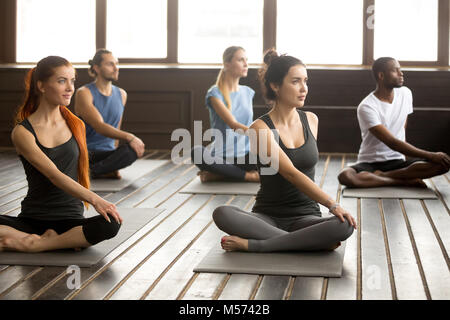Group of young sporty people sitting in parivritta sukhasana Stock Photo