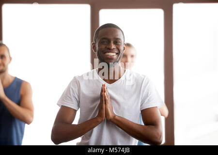 Smiling african-american man holding hands in namaste at group t Stock Photo