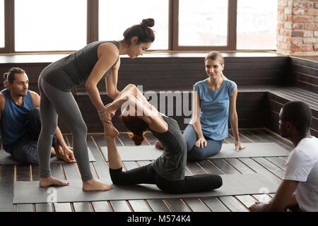 Female yoga instructor helping woman doing exercise at group tra Stock Photo
