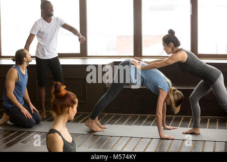 Yoga teacher assisting woman doing downward facing dog stretchin