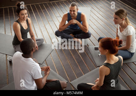 Diverse smiling people sitting on mats talking before yoga train Stock Photo