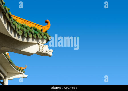 Chinese-inspired curved roof on a contemporary building with decorative glazed roof tiles and dragon shaped concrete beam against a deep blue sky.