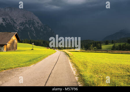 Smooth turning country road in alpine valley, thunderstorm Stock Photo