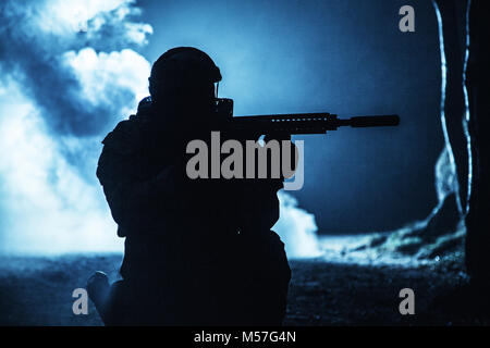 Black silhouette of soldier in the smoke moving in battle operation. Back light, cropped, toned and colorized Stock Photo