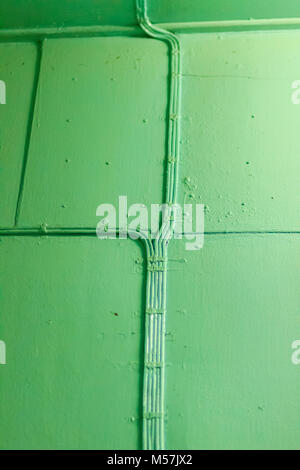 Old aqua wall crossed by an electric cable of the same color. The network of electrical cables on the old wall with fluorescent light Stock Photo