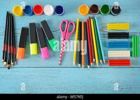 School supplies (scissors, paints, modelling clay, markers, pencils) on blue wooden background. Top view. Copy space. Stock Photo