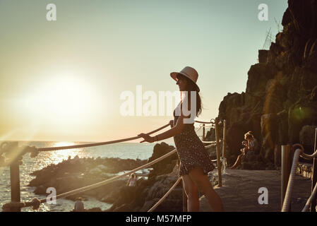 Tourist young girl in a skirt watching a beautiful dramatic sunset view by the sea Stock Photo