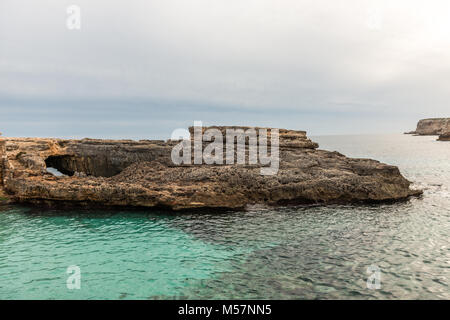 The sunset and a rock formation in the water of the mediterranean sea seen from the Caló des Moro on the island of Mallorca, Spain. Stock Photo