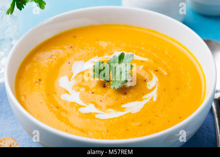 Pumpkin and carrot soup with cream and parsley on blue stone background. Close up. Stock Photo