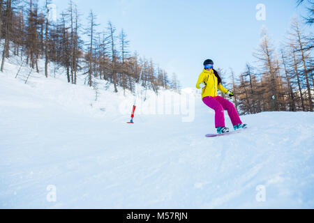 Picture of athlete woman wearing helmet and mask snowboarding from snowy slope with trees Stock Photo