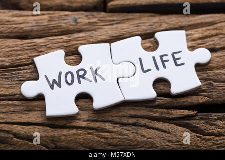 Closeup of work and life words written on pieces of jigsaw puzzle against wood Stock Photo