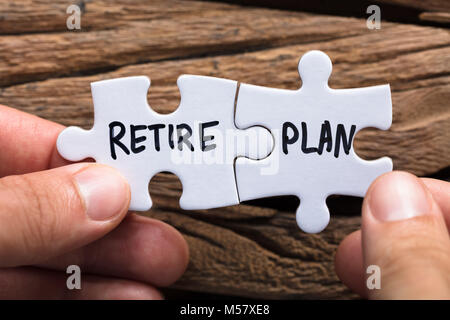 Closeup of hands holding retire plan matching jigsaw pieces against wood Stock Photo