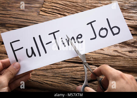 Closeup of hands cutting full-time job words on paper with scissors against wood Stock Photo