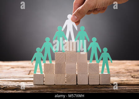 Closeup of hand placing paper businessman with employees on pyramid blocks Stock Photo