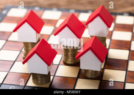 Closeup of house models on stacked coins on chessboard Stock Photo
