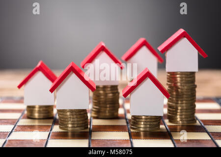 Closeup of small houses on stacked coins on chessboard Stock Photo