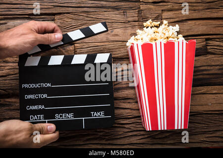 Closeup of hands holding clapperboard by popcorn on wood Stock Photo