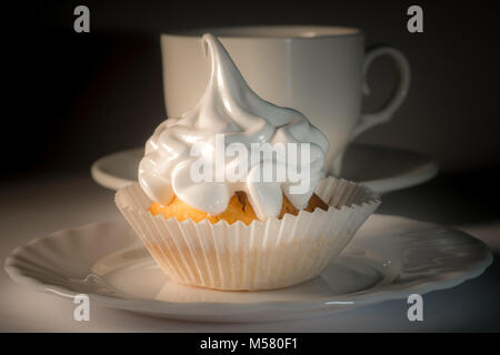 Cupcake with white icing on a plate and a cup of tea. Sweet dessert with white glaze close-up.Kapteyka and a cup of tea. Cupcake with icing. Stock Photo