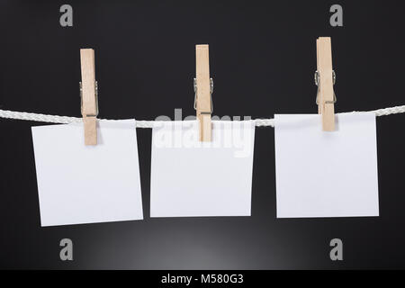 Closeup of white paper cards hanging on rope attached with clothespins against black background Stock Photo