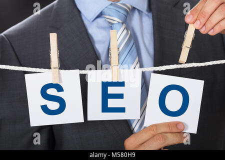 Closeup midsection of businessman pinning SEO cards on clothesline Stock Photo