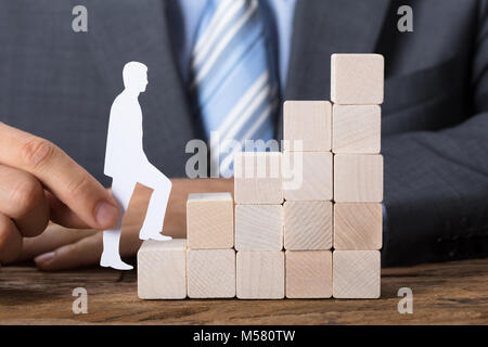 Closeup of businessman moving paper man upstairs made of wooden blocks on table Stock Photo