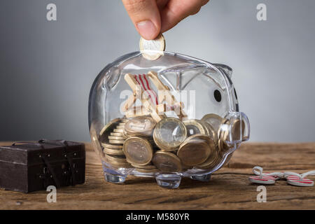 Closeup of hand putting coin in transparent piggy bank with deck chair Stock Photo