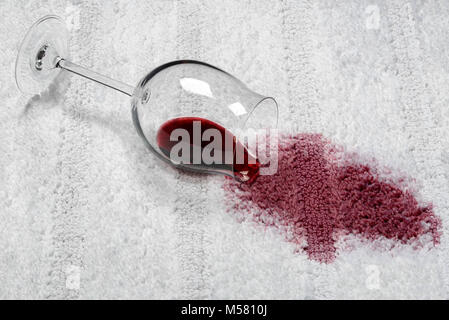 Fallen wineglass leaking a big red wine spill spot on white carpet Stock Photo