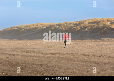 Running woman on sandy beach during morning hours Stock Photo