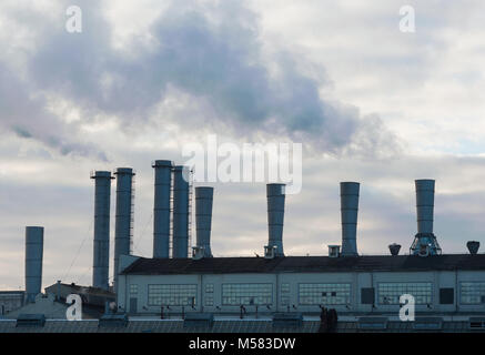 Smoke comes from industrial pipes against a cloudy sky. Stock Photo