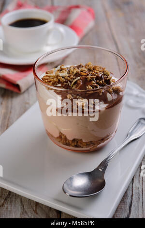 Yogurt with granola under chocolate sauce and a cup of black coffee on a rustic table Stock Photo