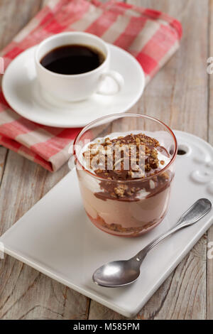 Yogurt with granola under chocolate sauce and a cup of black coffee on a rustic table Stock Photo