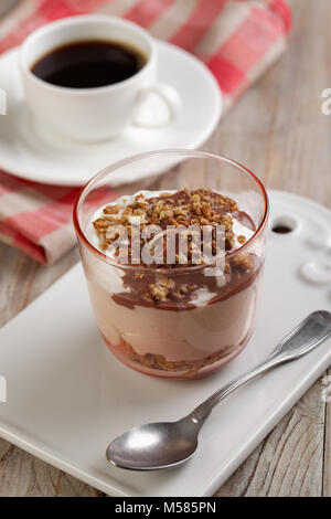 Yogurt with granola under chocolate sauce and a cup of black coffee on a rustic table Stock Photo