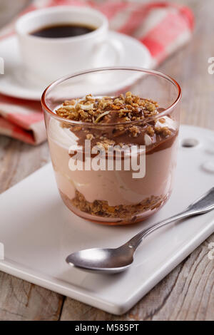 Yogurt with granola under chocolate sauce and a cup of black coffee on a rustic table Stock Photo
