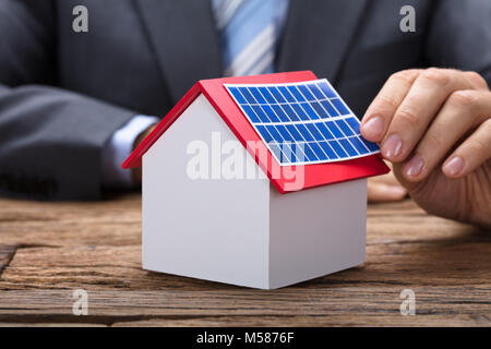 Midsection of businessman sticking solar panel on model home at wooden table Stock Photo