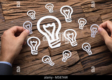 Cropped image of businessman arranging paper light bulbs on wooden table Stock Photo