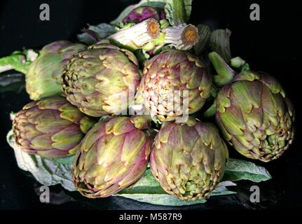 Beautiful fresh purple and green artichokes with green leaves on black background, close up Stock Photo