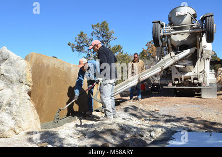 Grand Canyon National Park Bright Angel Trailhead Sign Pouring foundation. Crew pouring cement foundation for the trailhead sign. The sign consists of a 9’x5’x12” sandstone slab weighing approximately 3 tons with two ‘bookend’ boulders on either side. Each of the bookend boulders was sawn and chiseled to create a slot to help support the slab vertically. The boulder on the east side also serves as a bench. The sign is also supported by a concrete foundation. “Bright Angel Trailhead” is sandblasted into the slab. It’s sited to capture a background view of the canyon, and has space behind for hi Stock Photo