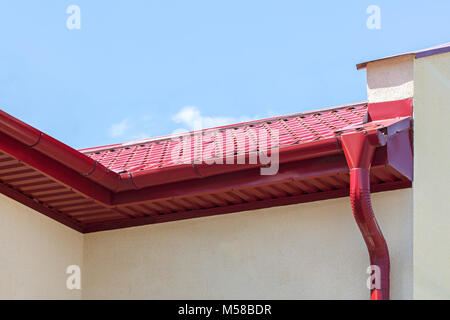 modern rain gutter with red metal downspout on house roof with blue sky in the background Stock Photo