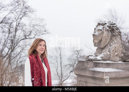 woman standing next to lion statue in city park in Milwaukee, Wisconsin in winter with snowflakes falling Stock Photo