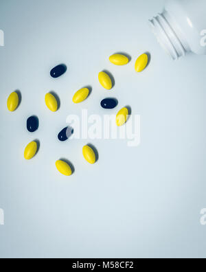 Yellow oval tablet pills and black tablets pills spilling out of pill bottle on white background with copy space for text. Global healthcare concept Stock Photo