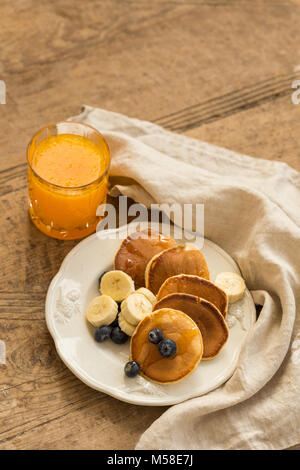 Pancakes with blueberries, banana and fresh orange juice over rustic wooden background. Stock Photo