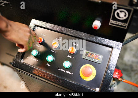 Black hand busy pushing red button on an industrial looking panel of switches for a coffee roasting machine Stock Photo